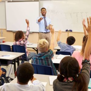 Teacher engaging students with raised hands in a classroom.