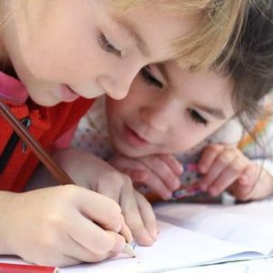 Two young children learning to write together, focused on a notebook.