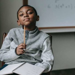 Young African American student with pencil in hand, thinking in a classroom setting.