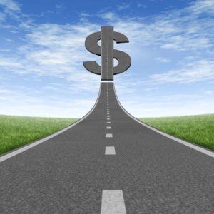 A long straight oad leading up to a large dollar sign under a blue sky.