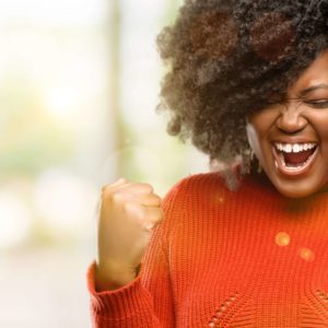 Beautiful african woman happy and excited celebrating victory expressing big success, power, energy and positive emotions. Celebrates new job joyful, outdoor