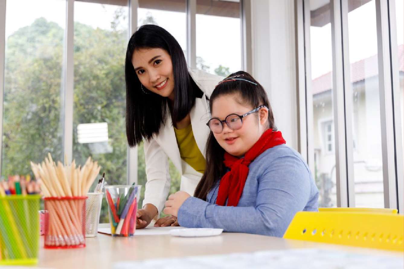 Smiling teacher helping a young girl with special needs with her schoolwork
