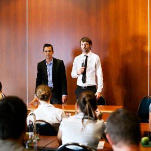 Business Presentation. Moderator and Speaker at business conference. Group of business people from behind sitting in seminar, listening the seminar - conference - training event presentators. Authentic, natural indoor light.