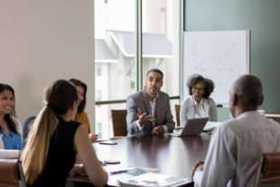 Mid adult businessman gestures as he discusses sales with a group of colleagues during a meeting.