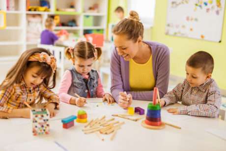 Happy female teacher teaching small kids how to draw at preschool.