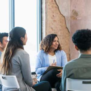 The diverse therapy group listens attentively as the young adult woman shares.