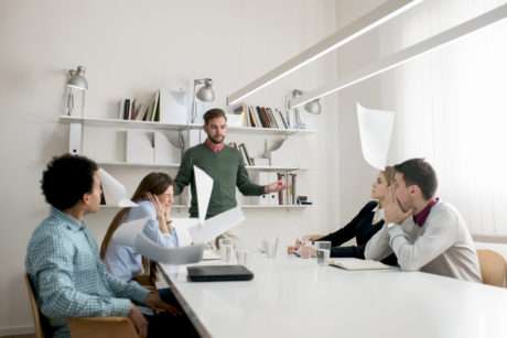 Unsatisfied manager throwing documents with the results of his employees while they're looking in shock.