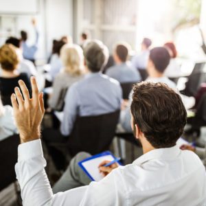 Back view of a businessman raising his hand on a seminar.