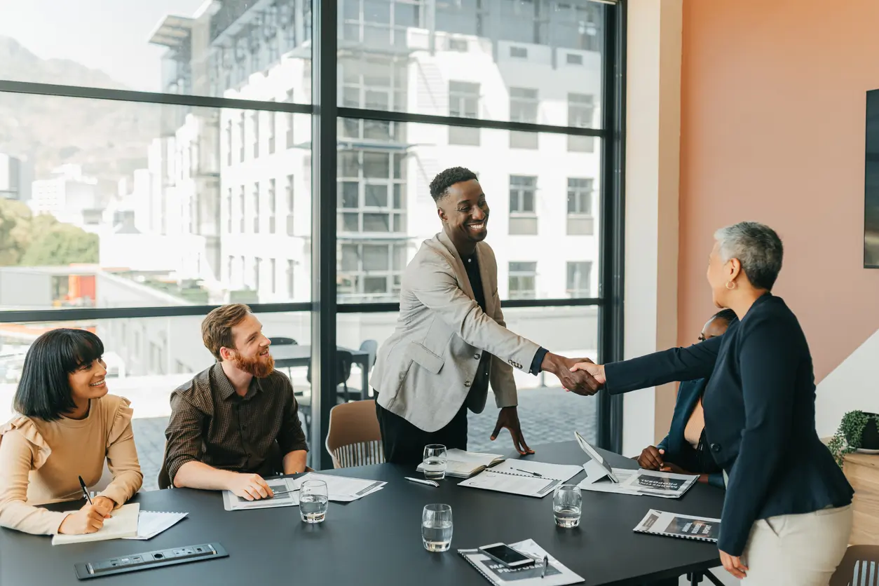Diverse business professionals shaking hands in a modern conference room meeting.