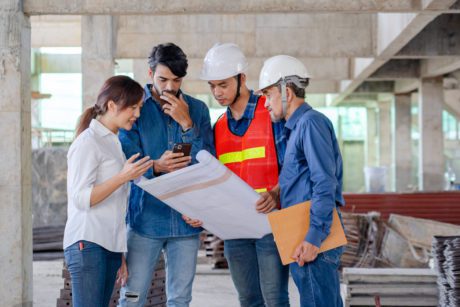 engineer foreman architect showing blueprint of house design to young couple owner