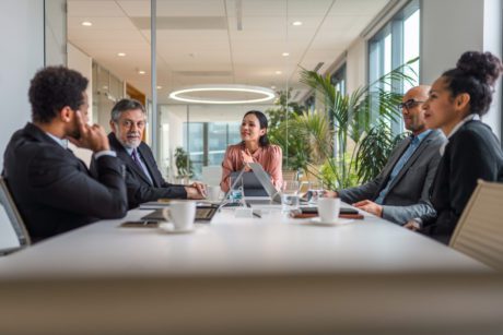 Multi-ethnic group of male and female executives sitting at conference table in modern office and exchanging ideas.