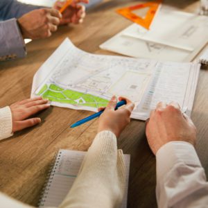 Close up shot of unrecognizable team of architects sitting around a table and reviewing plans and blueprints of a project they are designing.