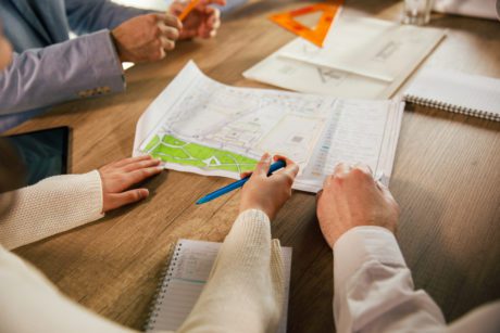 Close up shot of unrecognizable team of architects sitting around a table and reviewing plans and blueprints of a project they are designing.