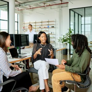 Diverse group in 20s and 30s wearing casual business attire, sitting together and conversing in modern open plan loft office.