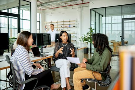 Diverse group in 20s and 30s wearing casual business attire, sitting together and conversing in modern open plan loft office.