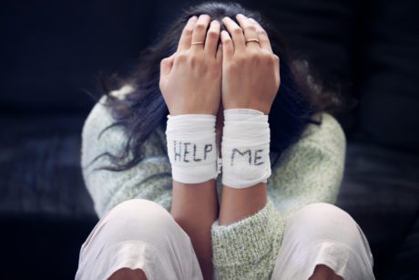Shot of a young woman with bandages wrapped around her wrists showing “help” written on them
